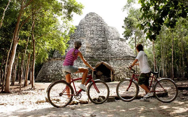 Two persons riding bicicle in front of Nohoch Mul, Coba. One of the destinations available for Cancun Airport Transportation