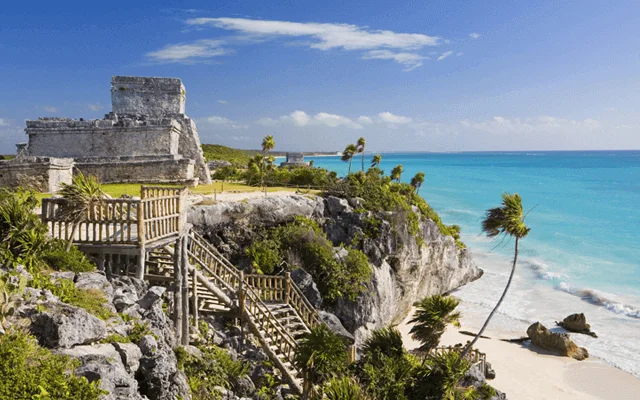 Tulum Mayan beachfront ruins on a sunny day, Tulum's public beach, ladders going from the Archaeological Site down to the beach, some mangrove and palm trees.