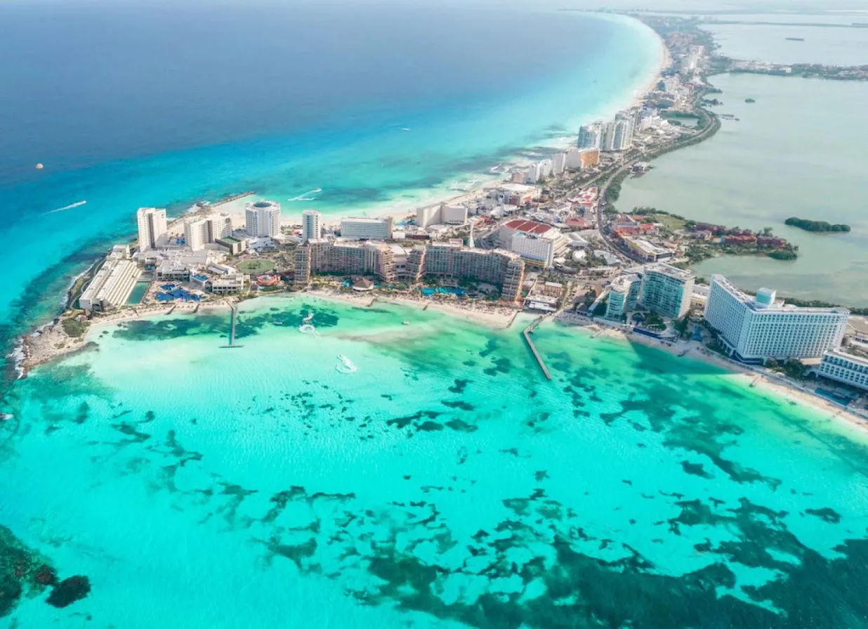 View of Cancun Hotel Zone beach with Beachfront Resorts, pools, calmed sea and bali beds.